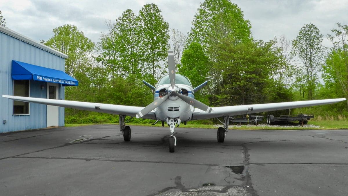 Front view of a white and blue Beechcraft Bonanza parked on the tarmac.