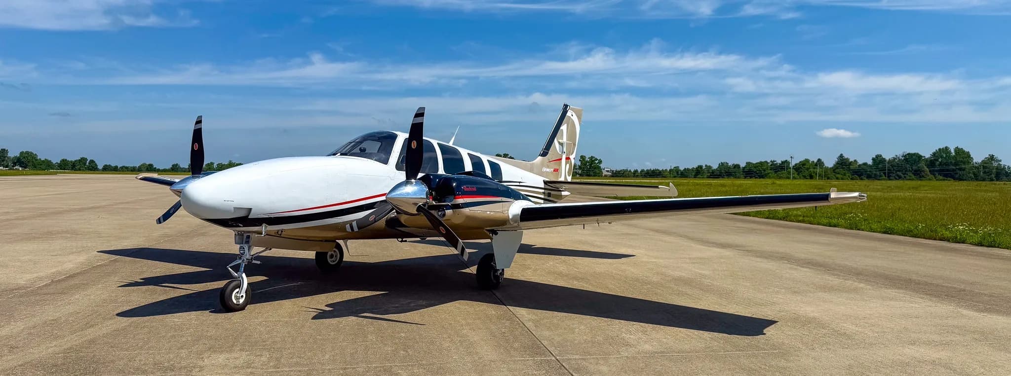 Three-quarter front view of a white and gold twin-engine Beechcraft Baron G58 parked on an airfield.