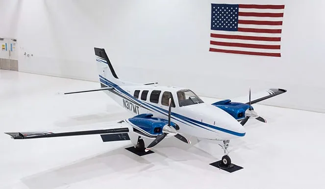Twin engine aircraft with a white and blue paint scheme in a hangar.