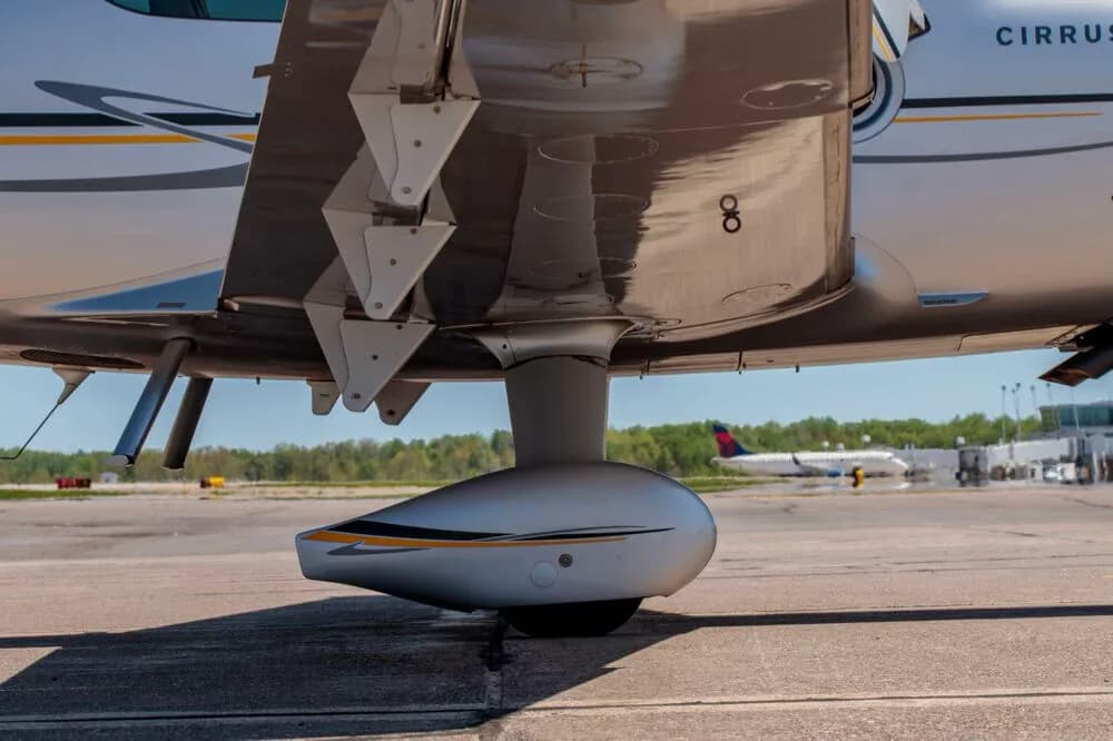 A close-up view of the main landing gear and the underside of the wing of the silver Cirrus SR22T aircraft.