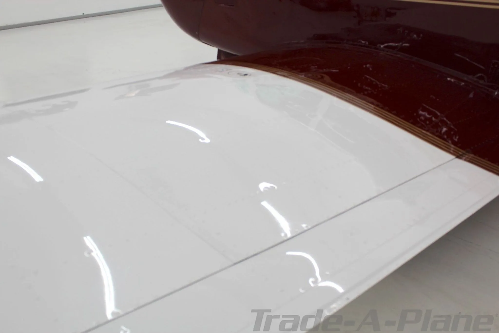 A close-up top view of the white section of the Mooney M20J's wing, showing reflections and rivets.