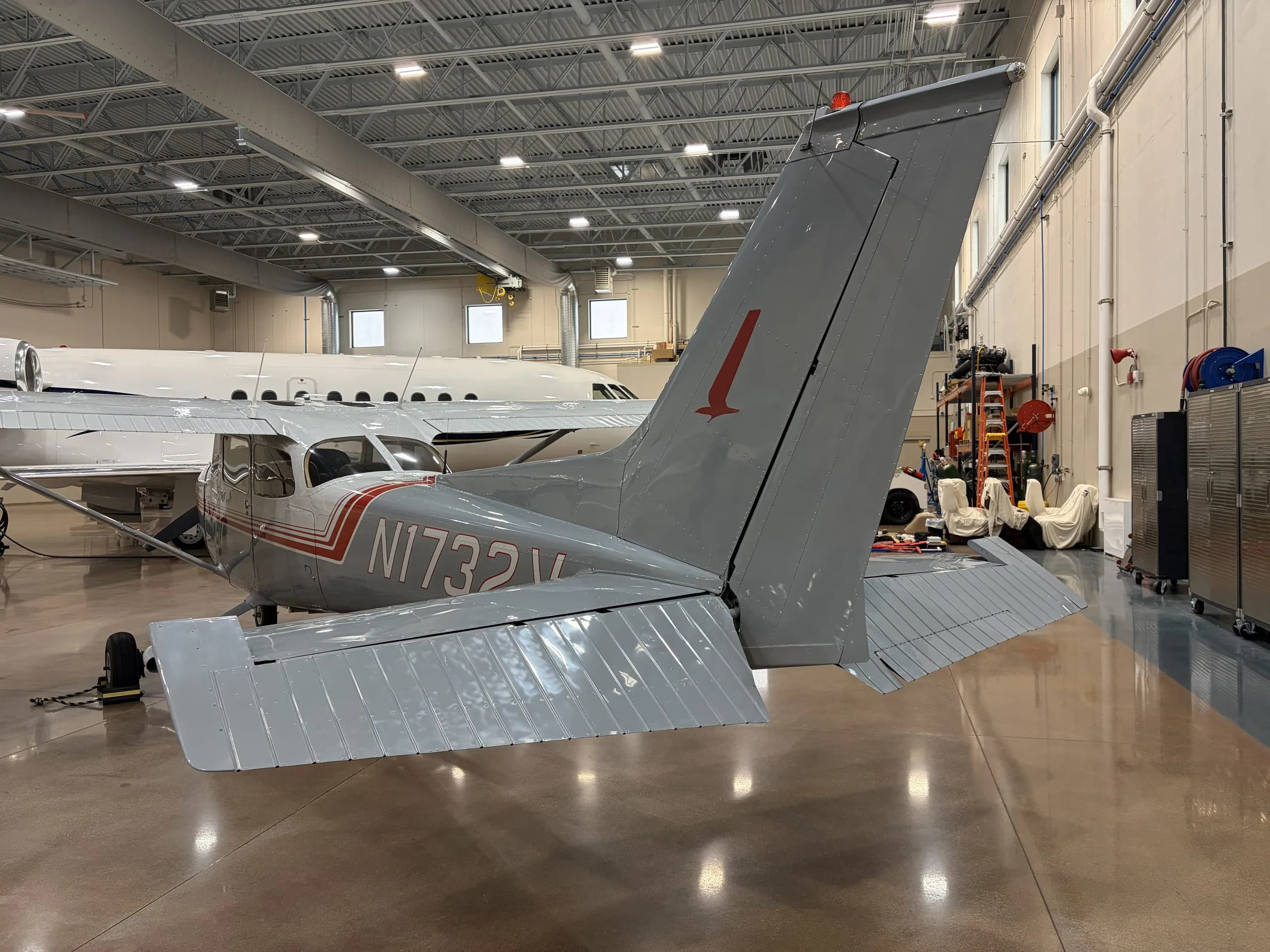 Rear view of a Cessna 172 with gray and red paint scheme in a hangar.