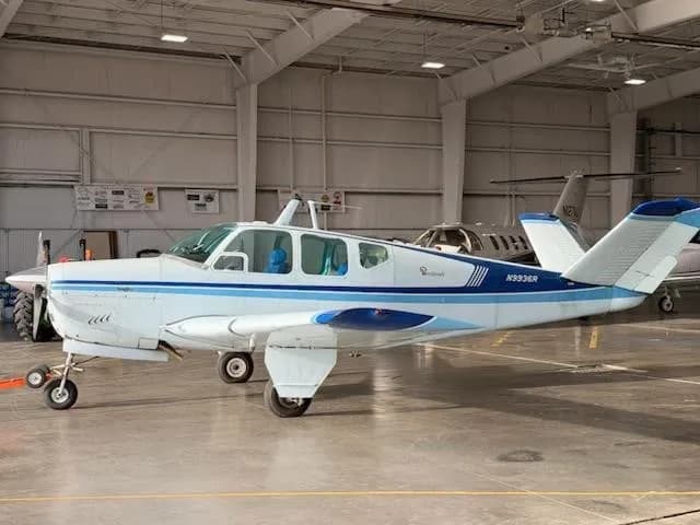A white and blue Beechcraft Bonanza N9936R parked in a hangar.