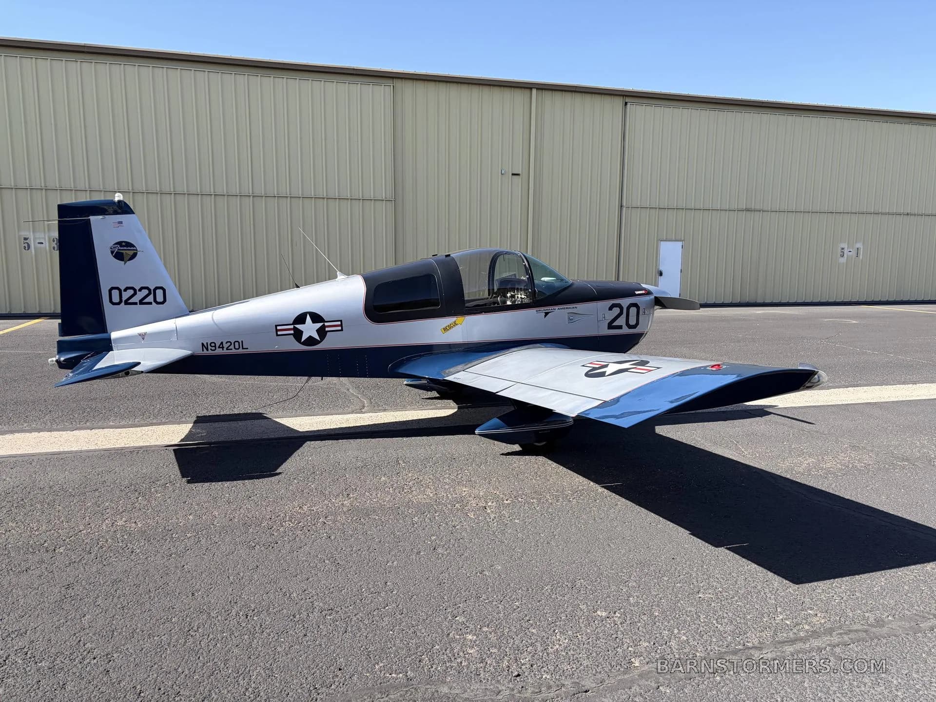 A side view of a silver and blue Grumman American AA-5 Traveler aircraft with tail number N9420L, parked on an airfield.