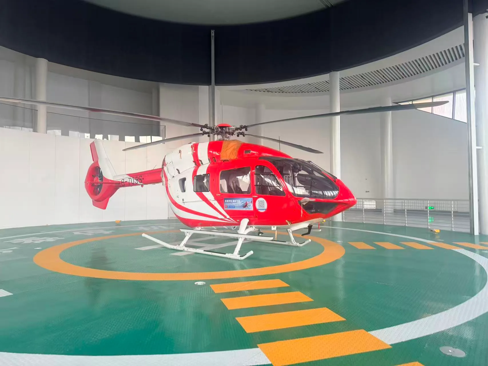 A red and white helicopter sits on a helipad inside a building.
