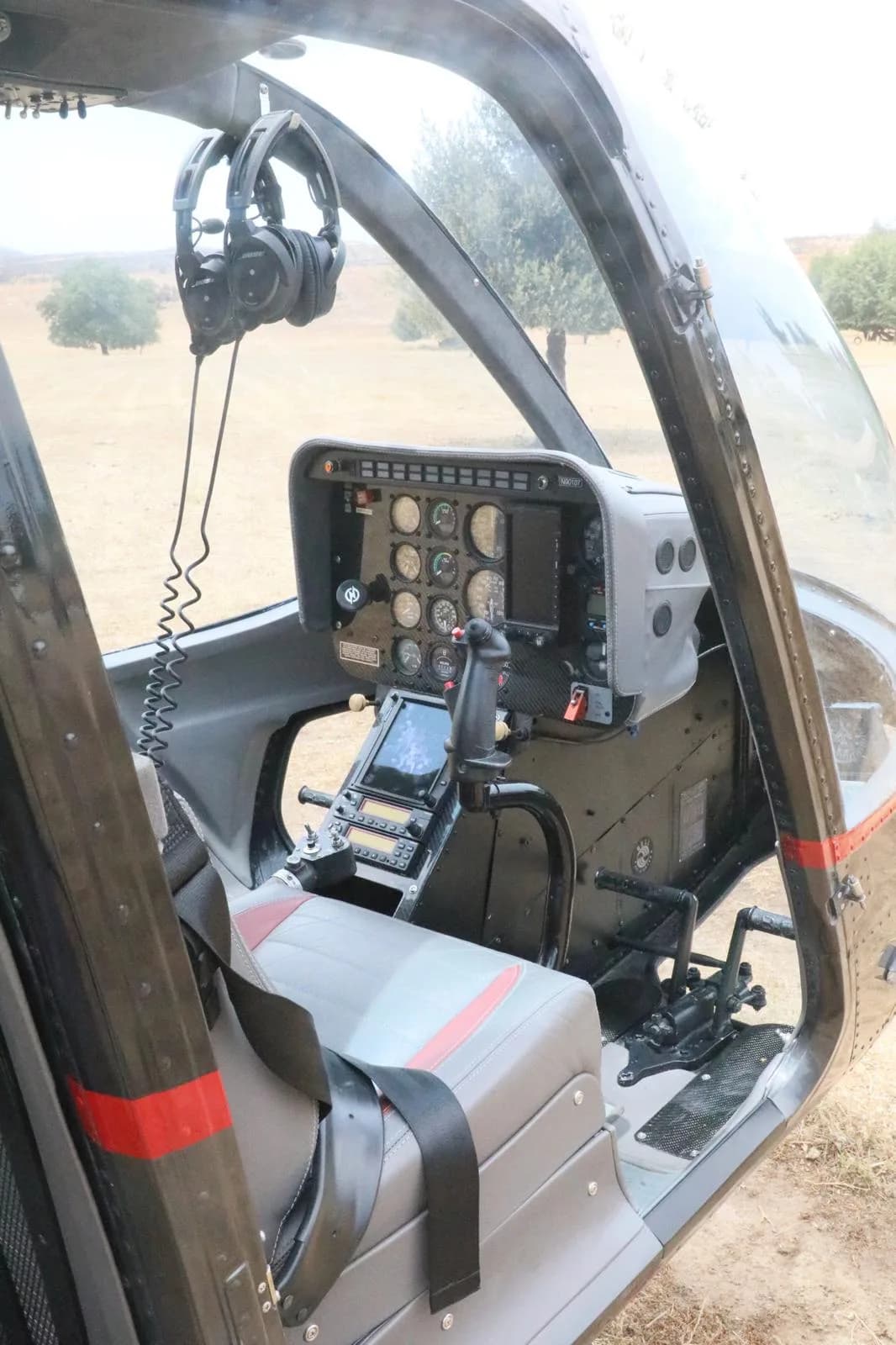 The cockpit of a black Bell 206 JetRanger helicopter showing the instrument panel, controls, and pilot's seat with headphones.