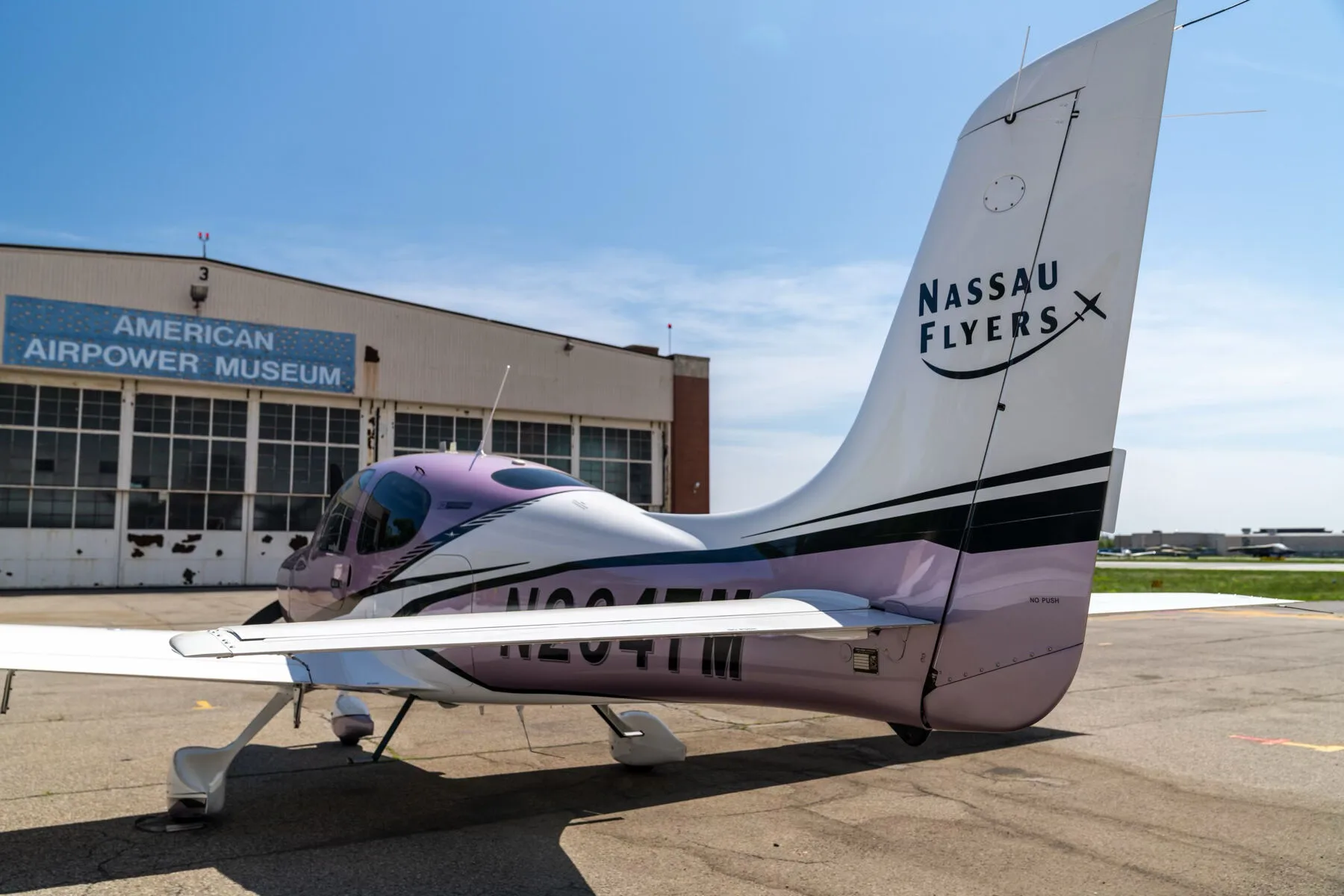A rear three-quarter view of the metallic lavender and white Cirrus SR22 aircraft, registration N264TM, showing the tail and wing.