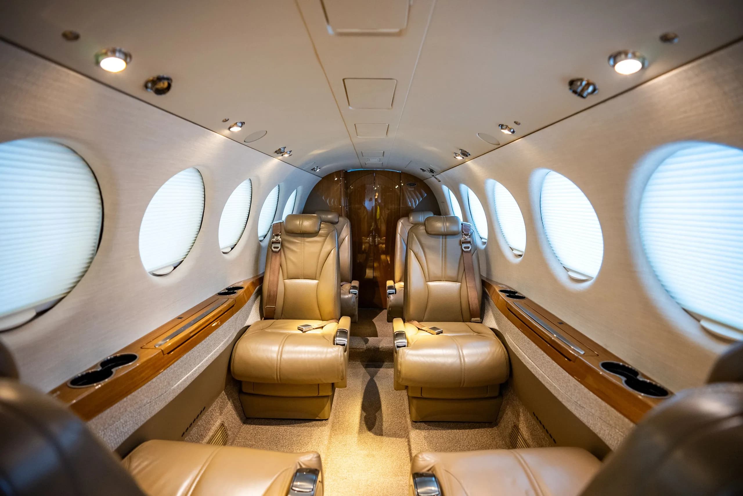 The luxurious cabin interior of an aircraft, featuring tan leather seats and large circular windows with shades.