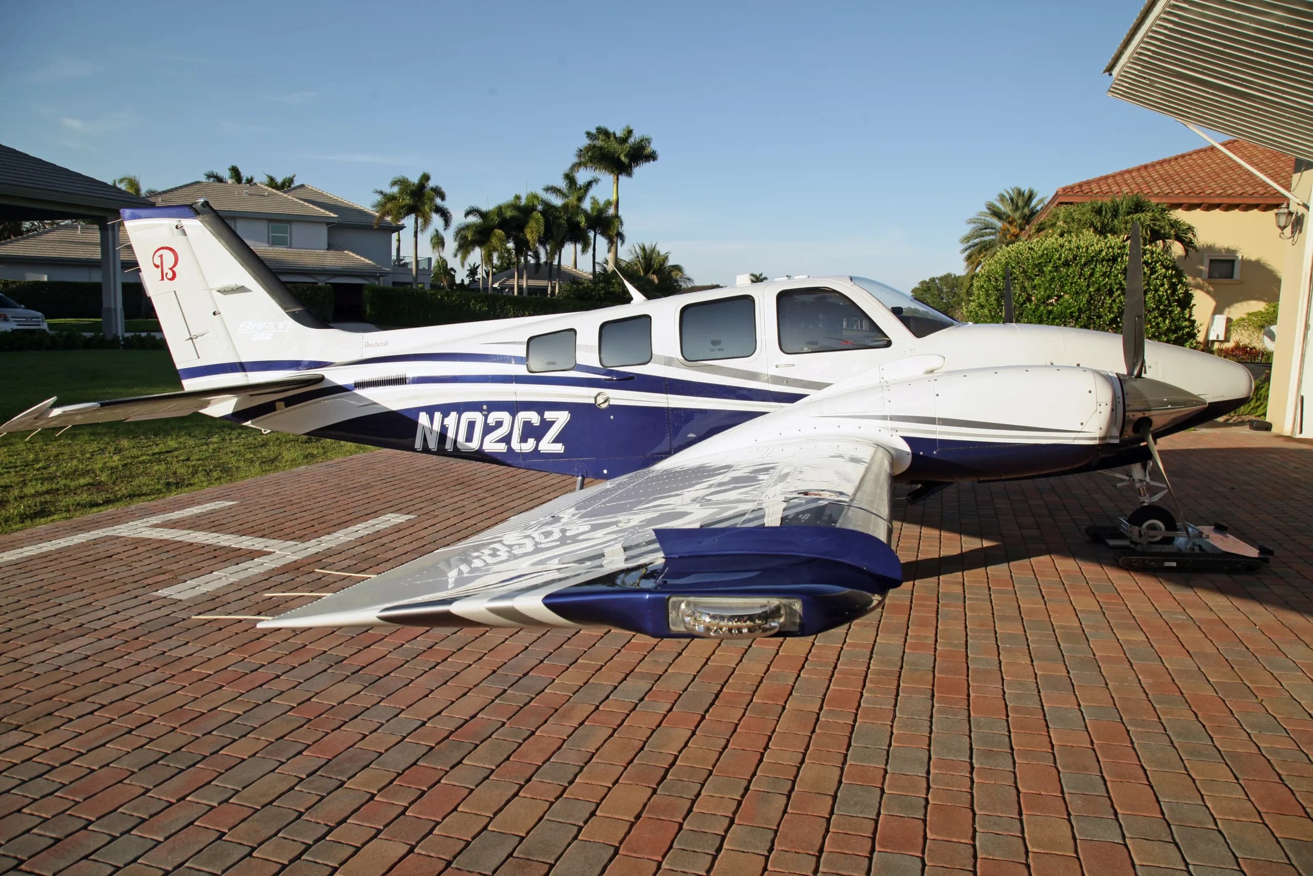 A white and blue Beechcraft Baron N102CZ parked on a paved driveway under a clear sky.