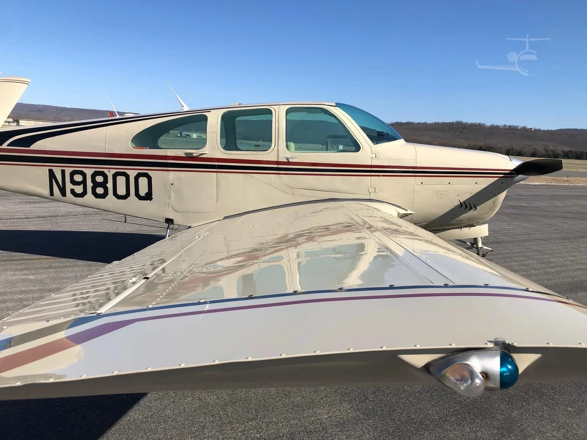 A close-up view of the wing and fuselage of the beige Beechcraft Bonanza N980Q, showing the navigation light and paint scheme.
