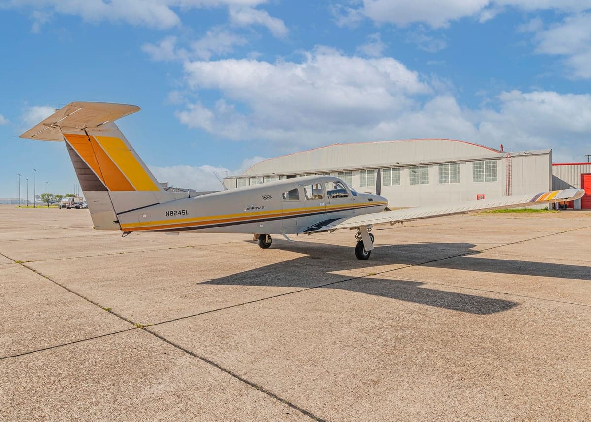 Piper Arrow II with N8245L tail number parked on the tarmac in front of a hangar.