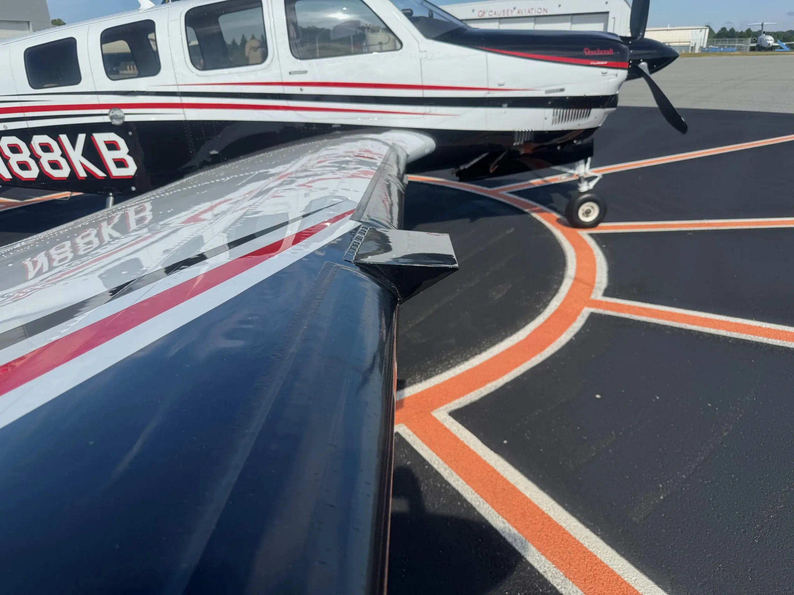 A close-up view of the wing and fuselage of a white and black Beechcraft Bonanza, showing the N88KB tail number reflection.