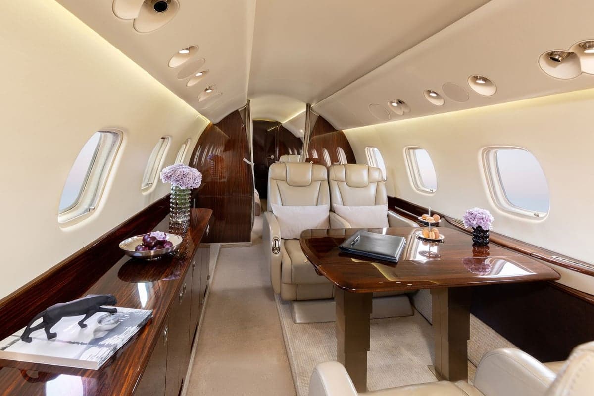 View of the Embraer Legacy 500 cabin with a table, leather seats, and wood trim.