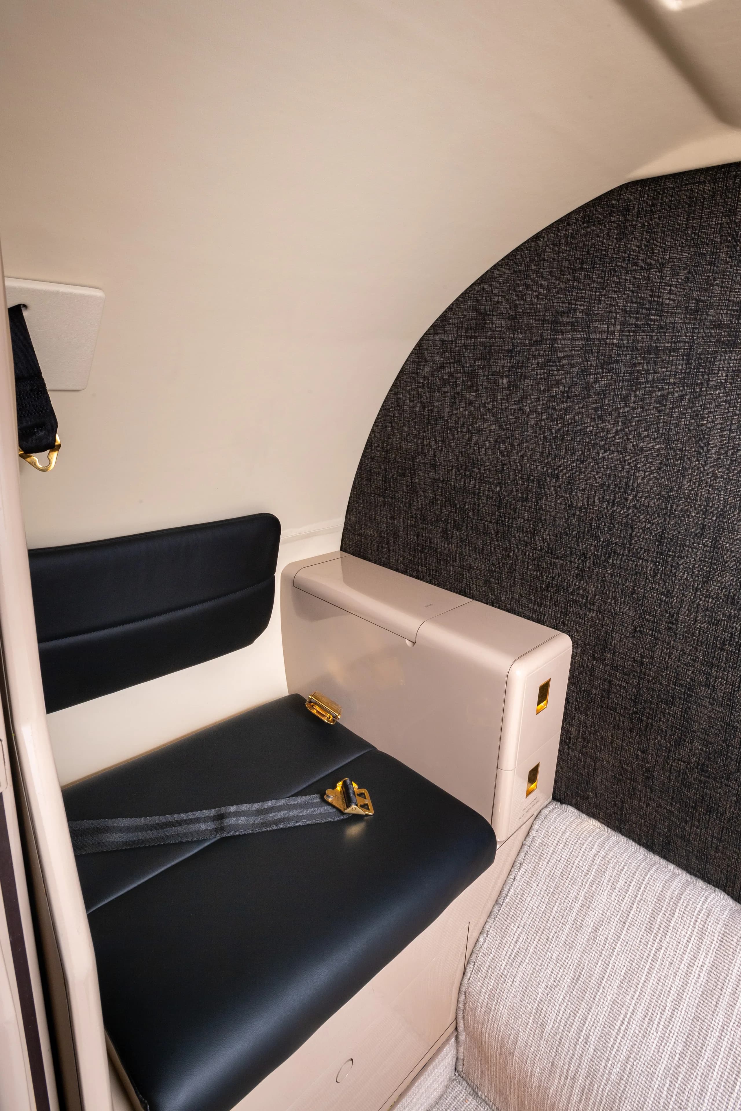 A close-up of a single black leather seat with a seatbelt and a small storage compartment in the business jet's cabin.