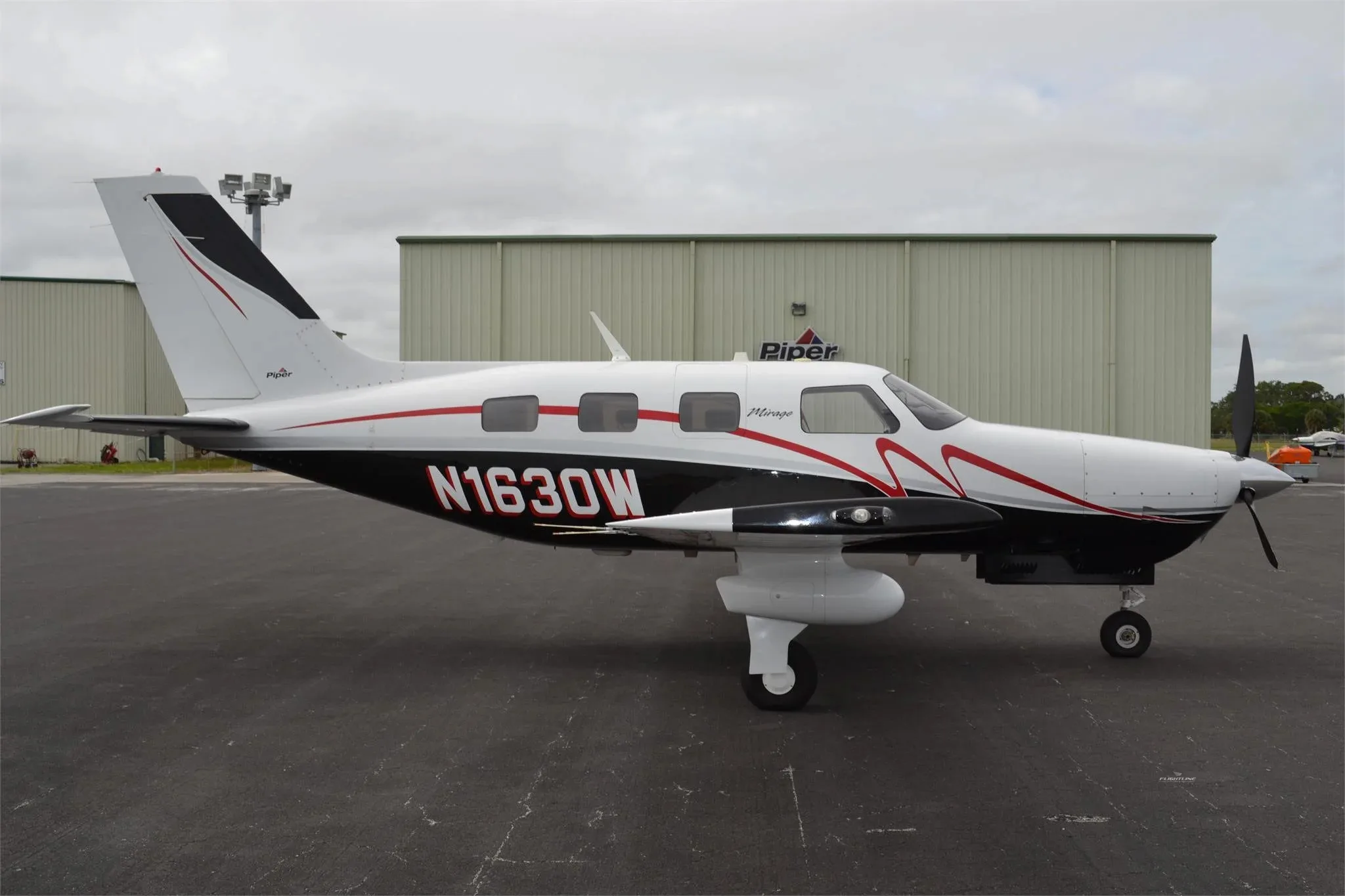 A side profile of the Piper Mirage N1630W, painted white, black, and red, parked on an asphalt apron.