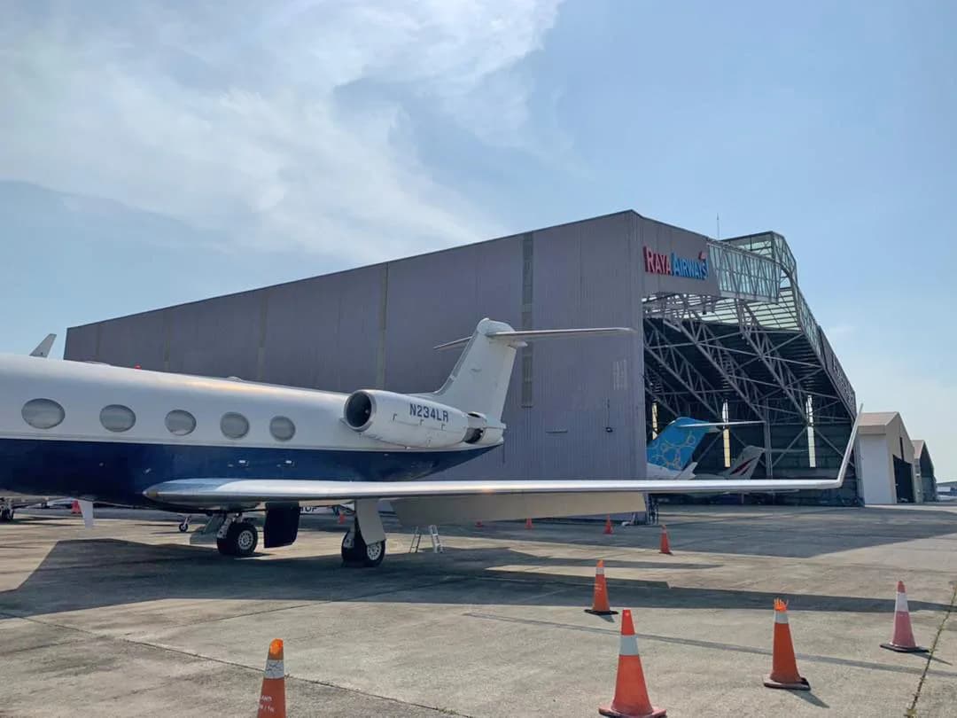 A Gulfstream G-IV business jet, registration N234LR, in a white and dark blue paint scheme, parked on a tarmac next to a large hangar.