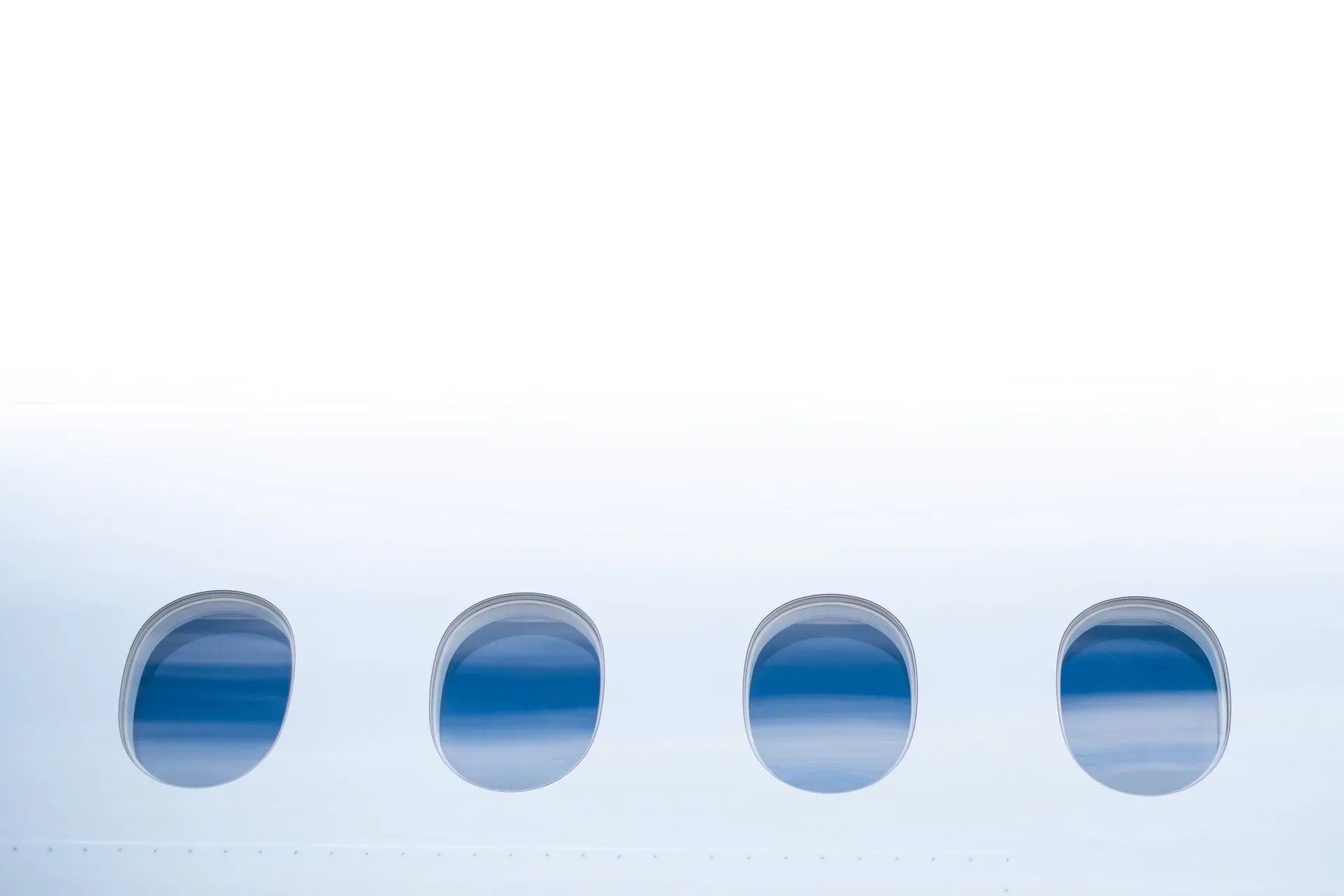 Four oval passenger windows on the side of a white aircraft, showing blue sky outside.