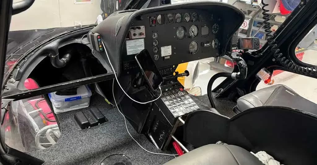 A wide view of the helicopter cockpit showing the instrument panel, controls, and a tablet.