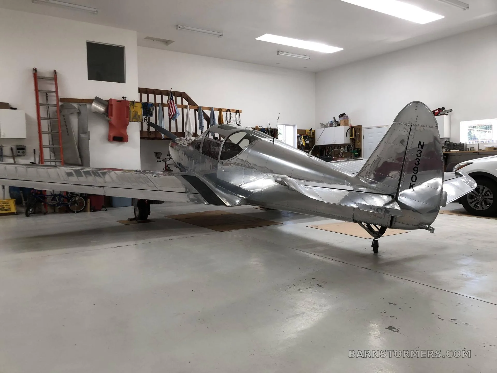 A shiny silver single-engine aircraft with tail number N3390K is parked inside a well-lit hangar.