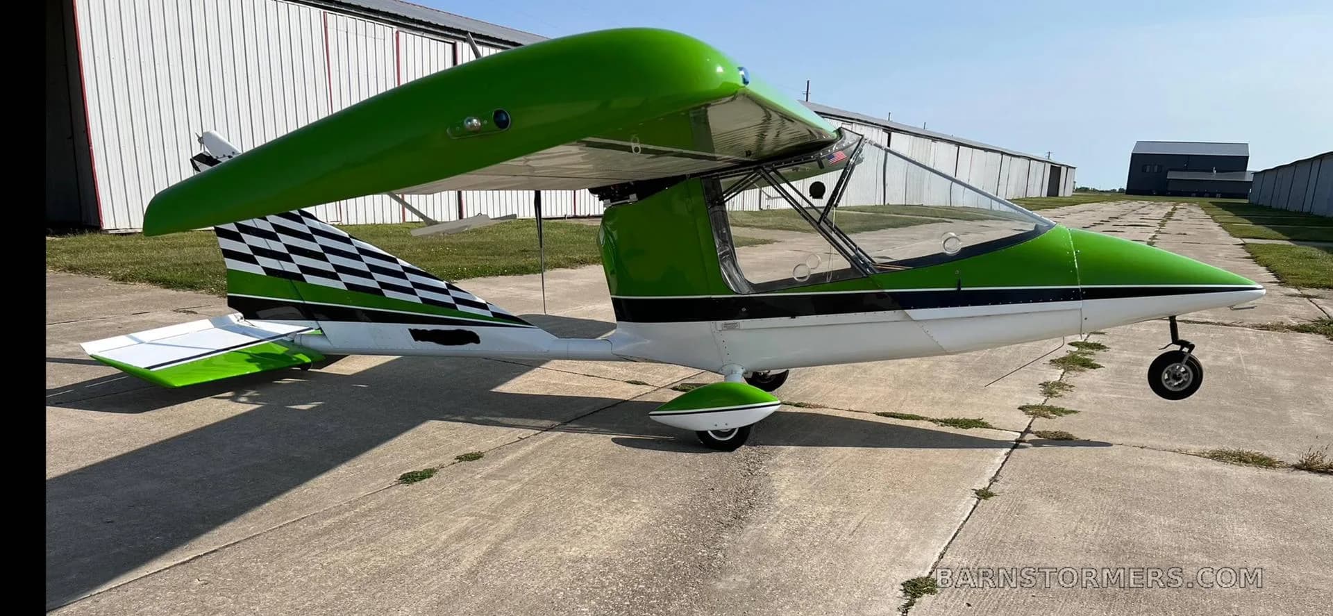 A bright green and white ultralight aircraft with a checkered tail is parked on a concrete tarmac outdoors.