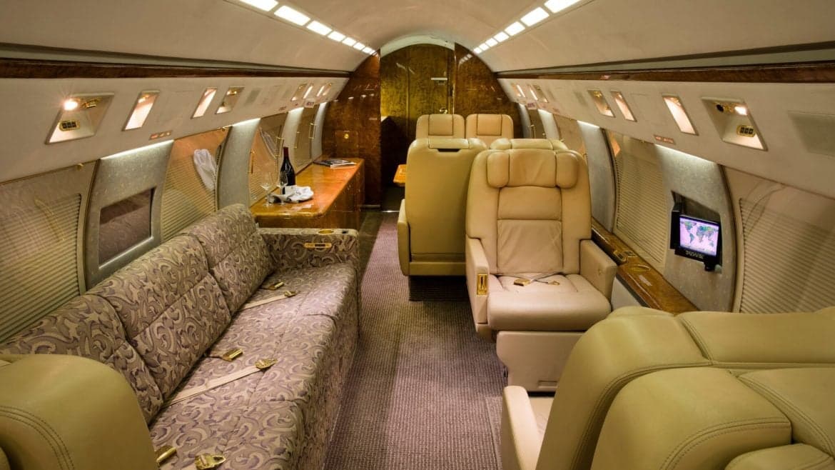 Wide view of the aircraft's interior with a sofa, leather seats, and wooden accents.