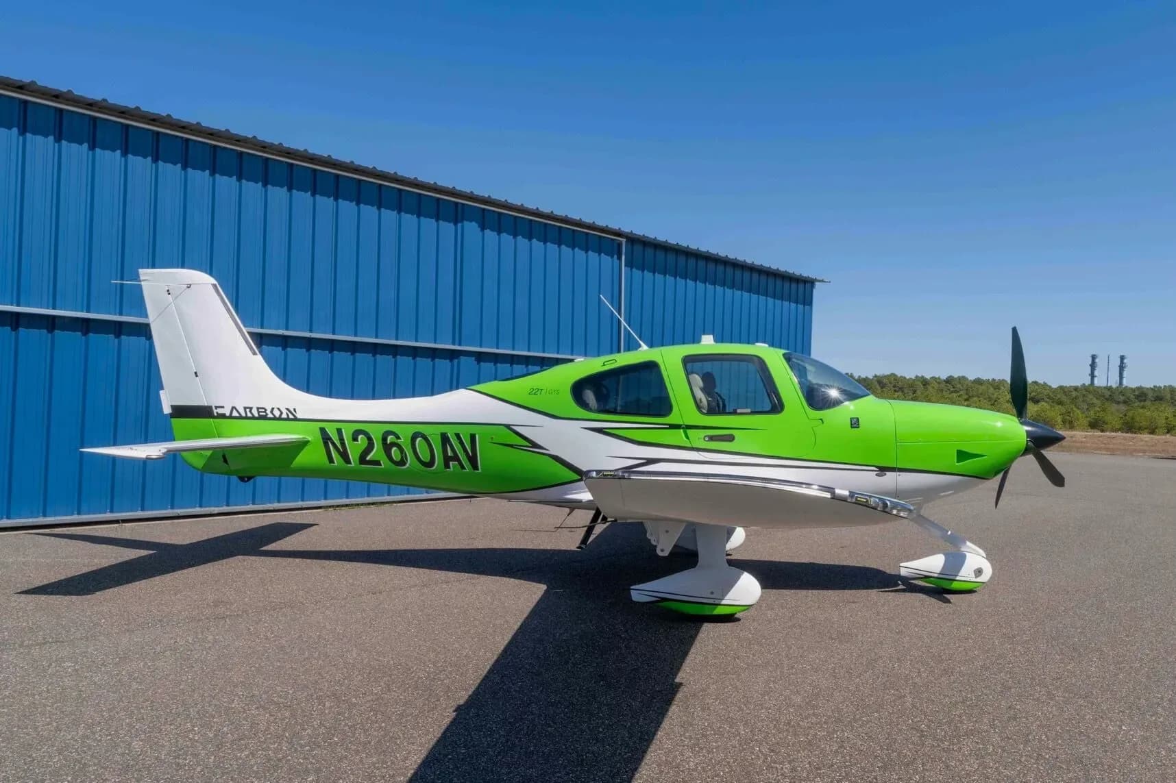 A bright green and white Cirrus SR22T aircraft, registration N260AV, parked on an asphalt ramp next to a blue hangar.