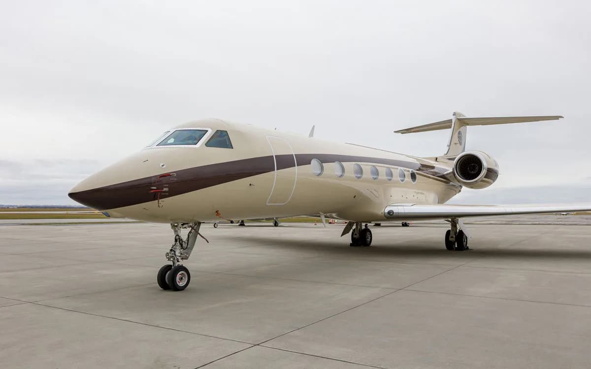 A tan and brown Gulfstream business jet is parked on an airport tarmac under an overcast sky.