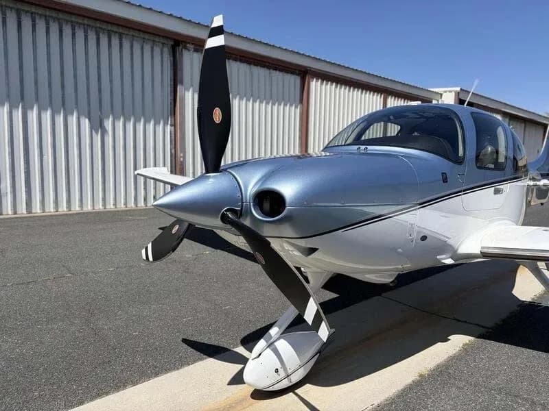 A close-up front view of the propeller and nose of a blue and white Cirrus SR22 aircraft.