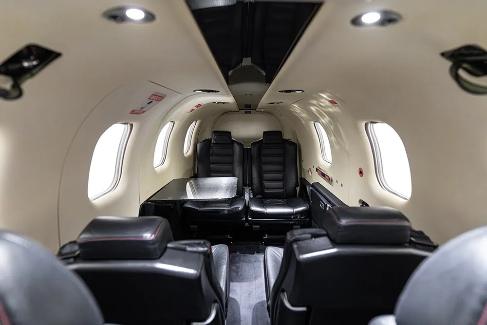 A perspective view down the TBM 930 cabin aisle, showing multiple black leather seats and a table.