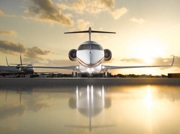 Front view of a white and gold aircraft parked on a reflective surface at sunset.