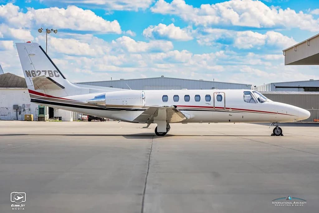 A side profile of a white Cessna Citation Bravo business jet with red and black stripes on the tarmac.