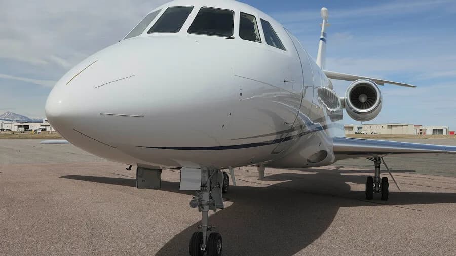 A close-up front view of a white business jet with blue stripes parked on an airfield.