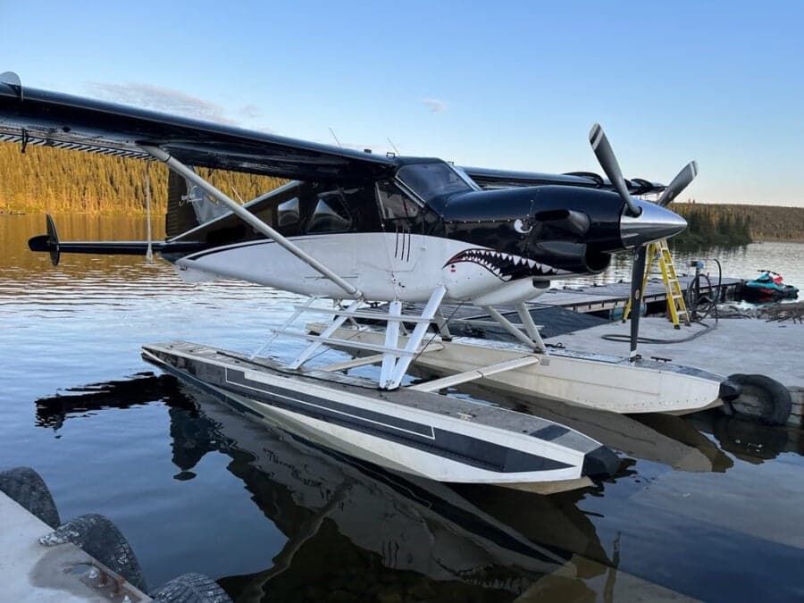 Seaplane with shark teeth paint scheme docked on a lake at dusk.