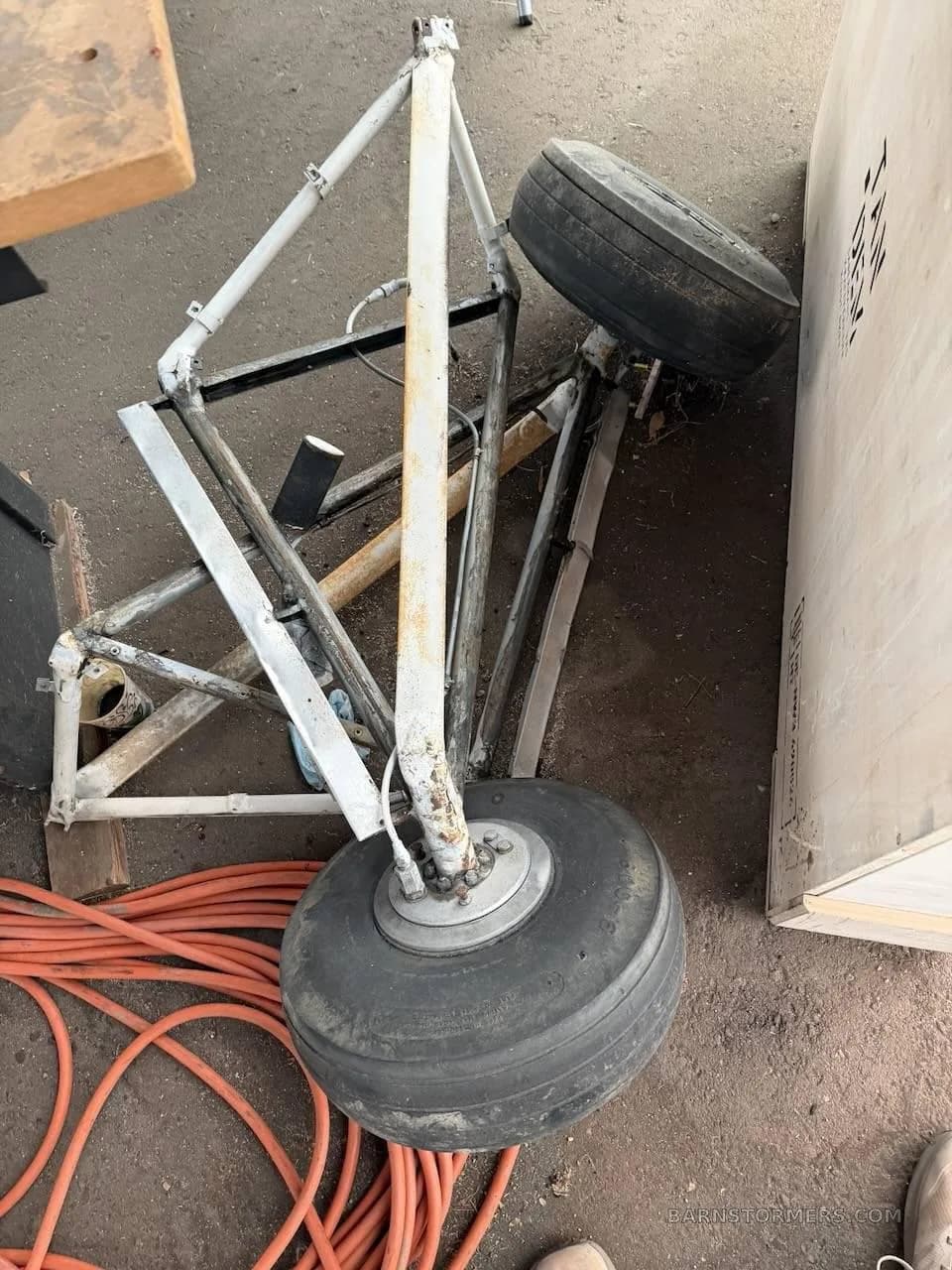 Two aircraft landing gear wheels and strut assemblies resting on a concrete floor with orange cables.