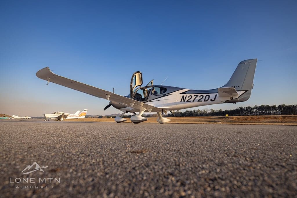 A Cirrus SR22T aircraft is parked on the tarmac with other aircraft in the background.