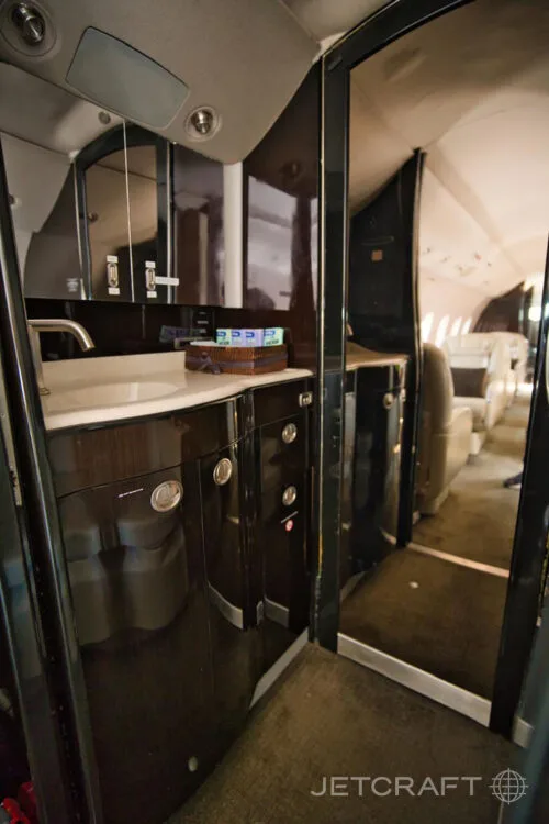 A view of an aircraft galley or lavatory area with a sink, dark wood cabinetry, and a glimpse of the cabin beyond.