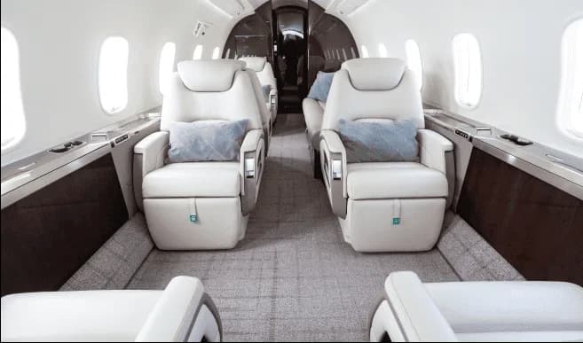 The luxurious interior cabin of a private jet features light-colored leather seats and a patterned carpet.