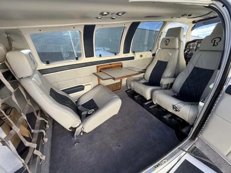 The aircraft's cabin interior showing four grey and black quilted seats, a fold-out table, and cargo netting.