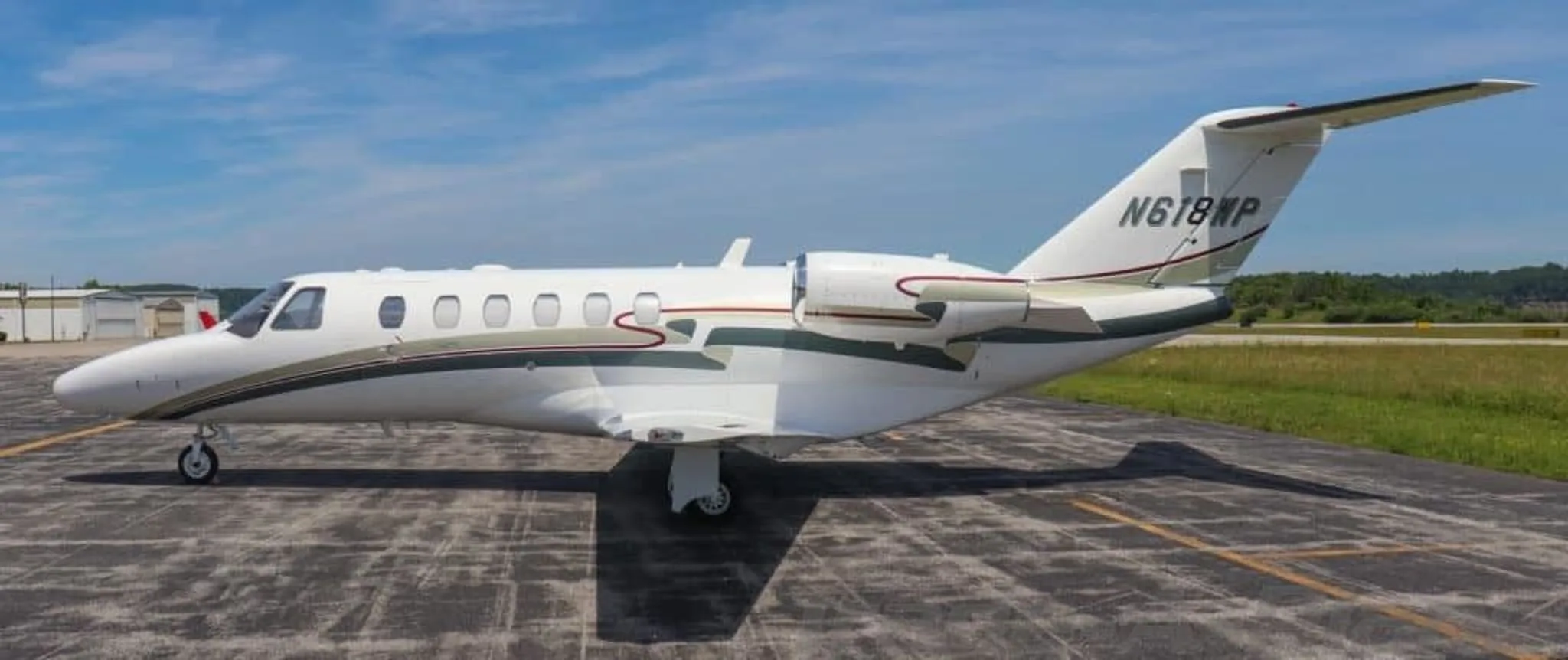 A side profile view of a white Cessna Citation CJ2+ business jet with green and red stripes parked on an airfield.
