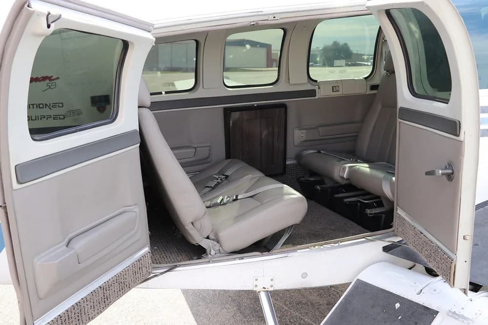 The light gray interior cabin of a Beechcraft Baron 58 with the passenger door open.