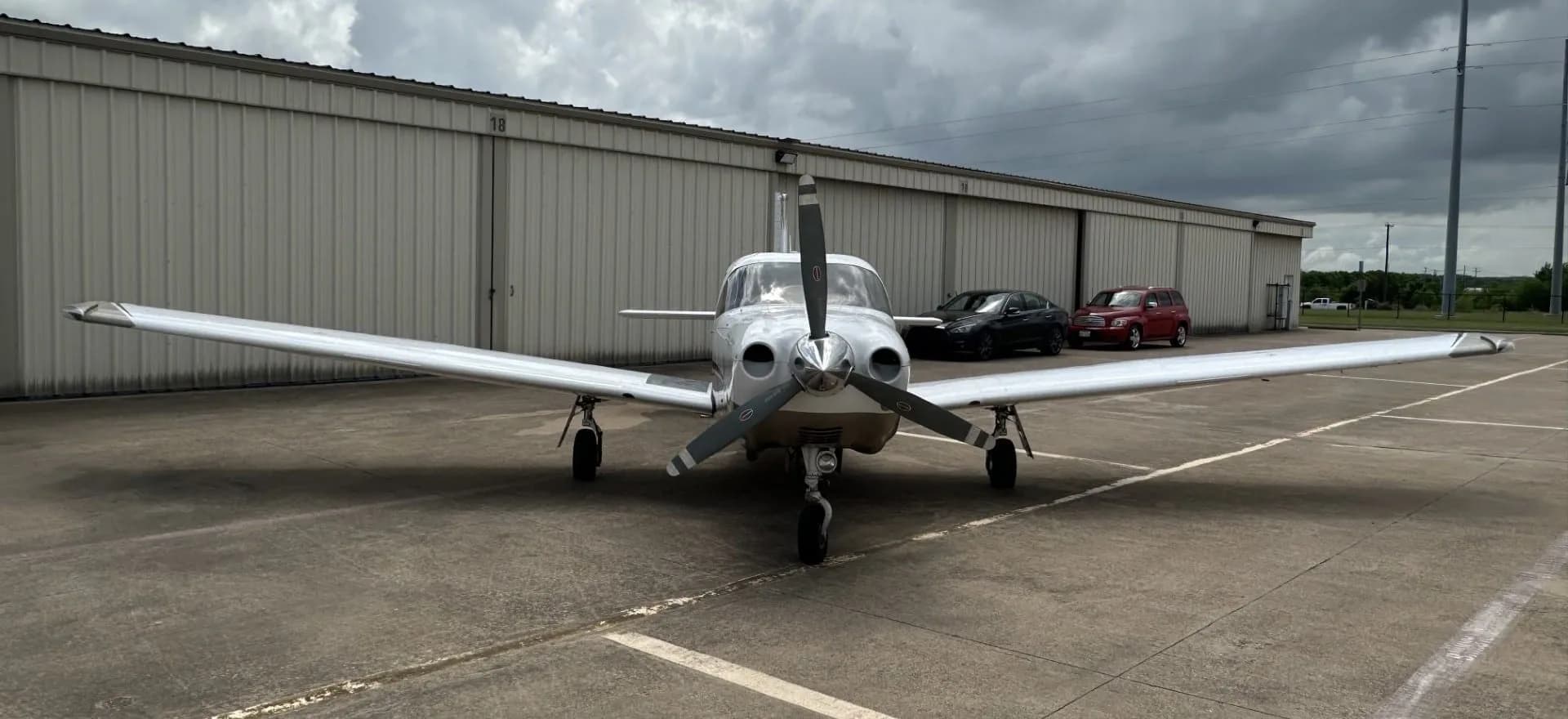 A white and tan Piper Saratoga II TC aircraft (N759C) seen from the front, parked on an asphalt ramp in front of hangars.