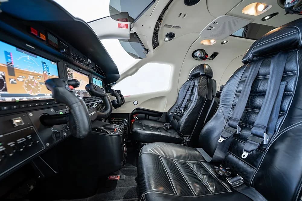 A close-up view of the TBM 930 cockpit with black leather pilot seats and multiple display screens.
