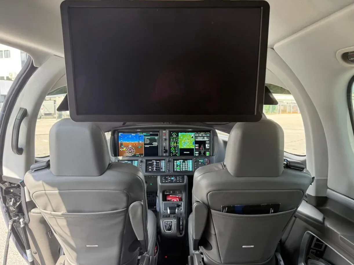View from the cabin looking forward into the cockpit of a Cirrus Vision Jet, showing the instrument panel and a large overhead screen.