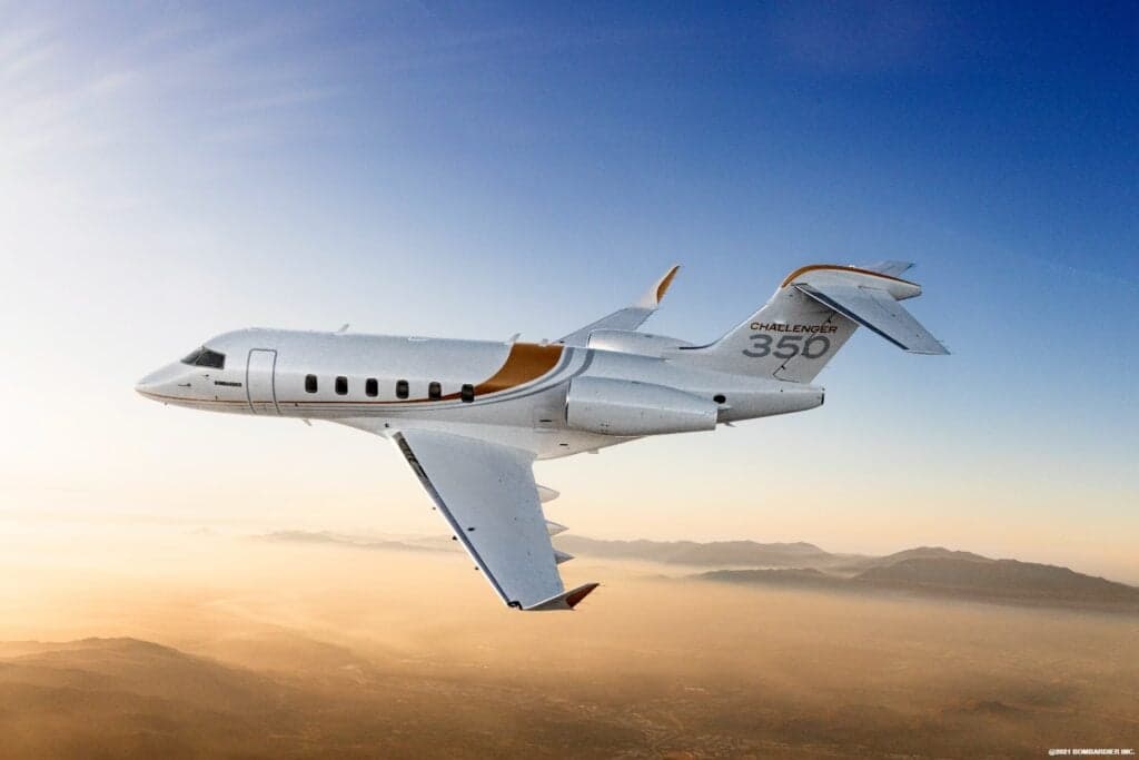 A Bombardier Challenger 350 in flight over a mountainous landscape.