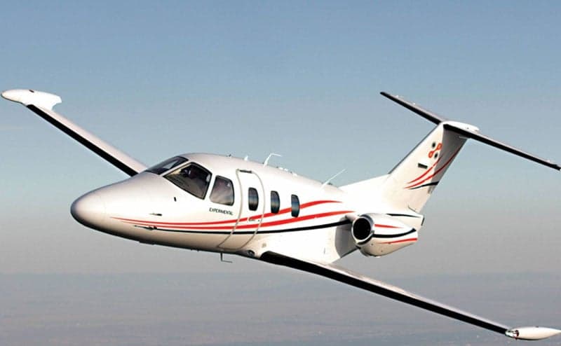 A white and red experimental jet aircraft is in flight against a clear blue sky.