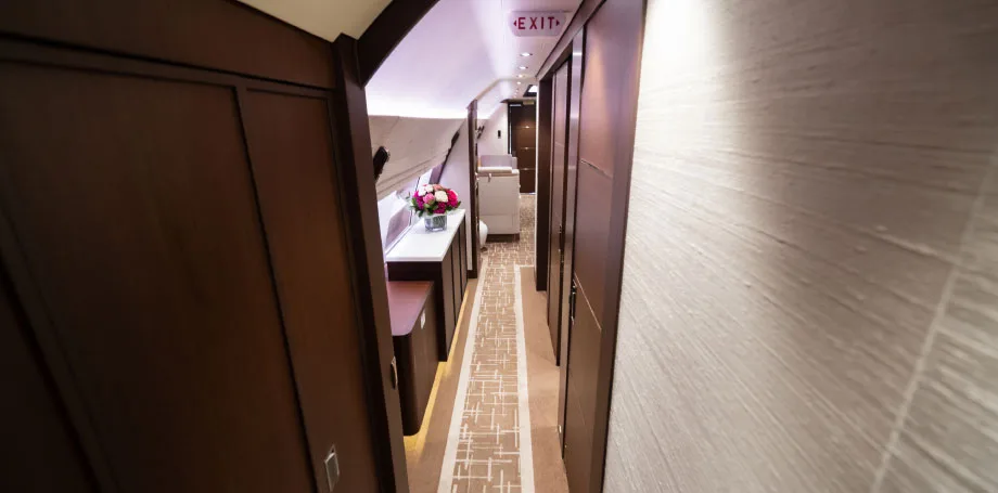 A luxurious aircraft interior hallway with dark wood paneling, a patterned carpet, and a small table with flowers.