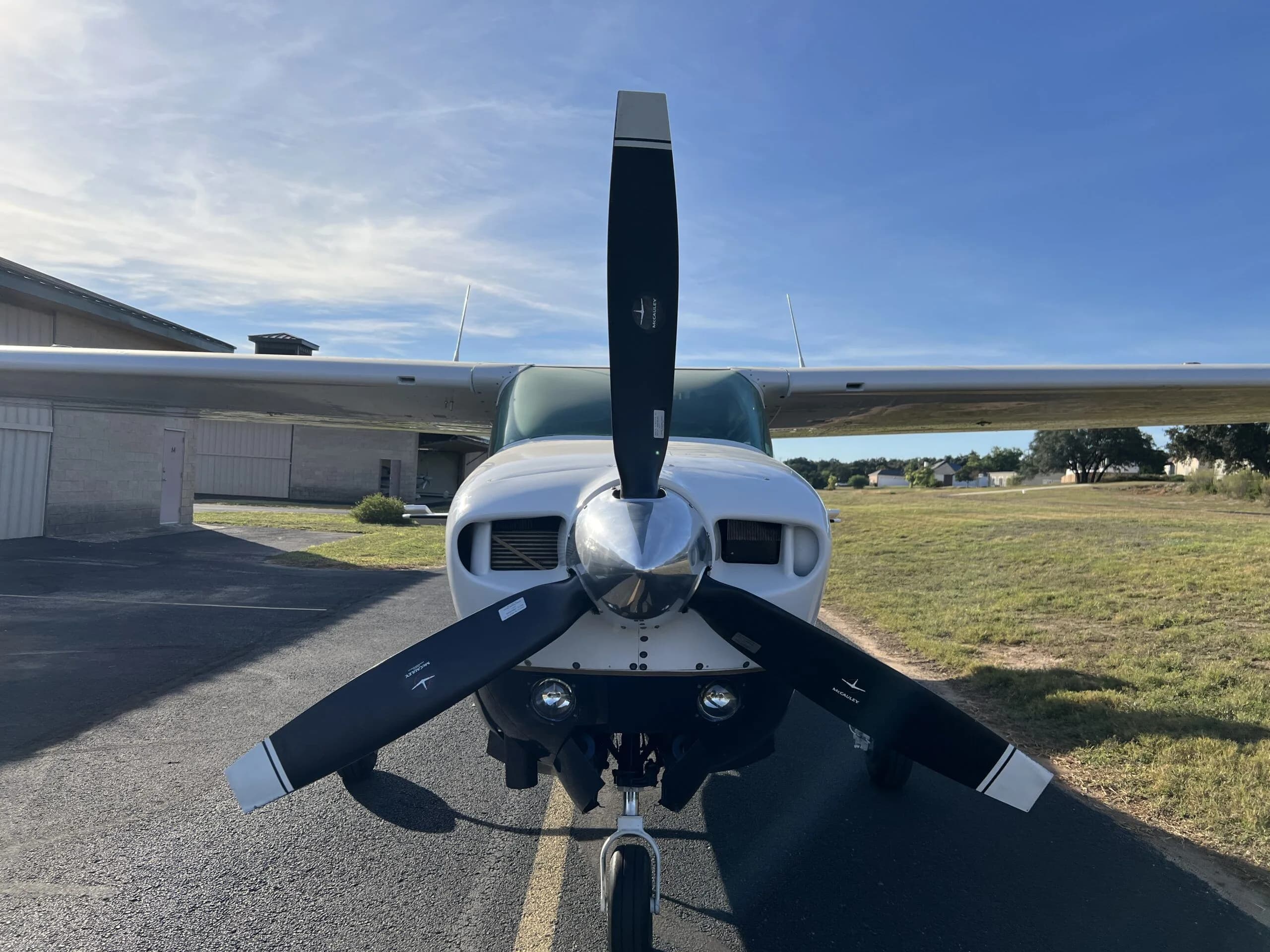 A head-on view of the white and blue Cessna 210, N58MA, with its propeller stationary, on an asphalt taxiway.