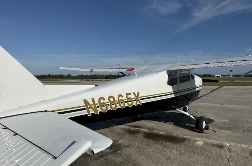 A side view of the rear fuselage of a white and black Cessna 172 with registration N6865X, parked on an airfield.
