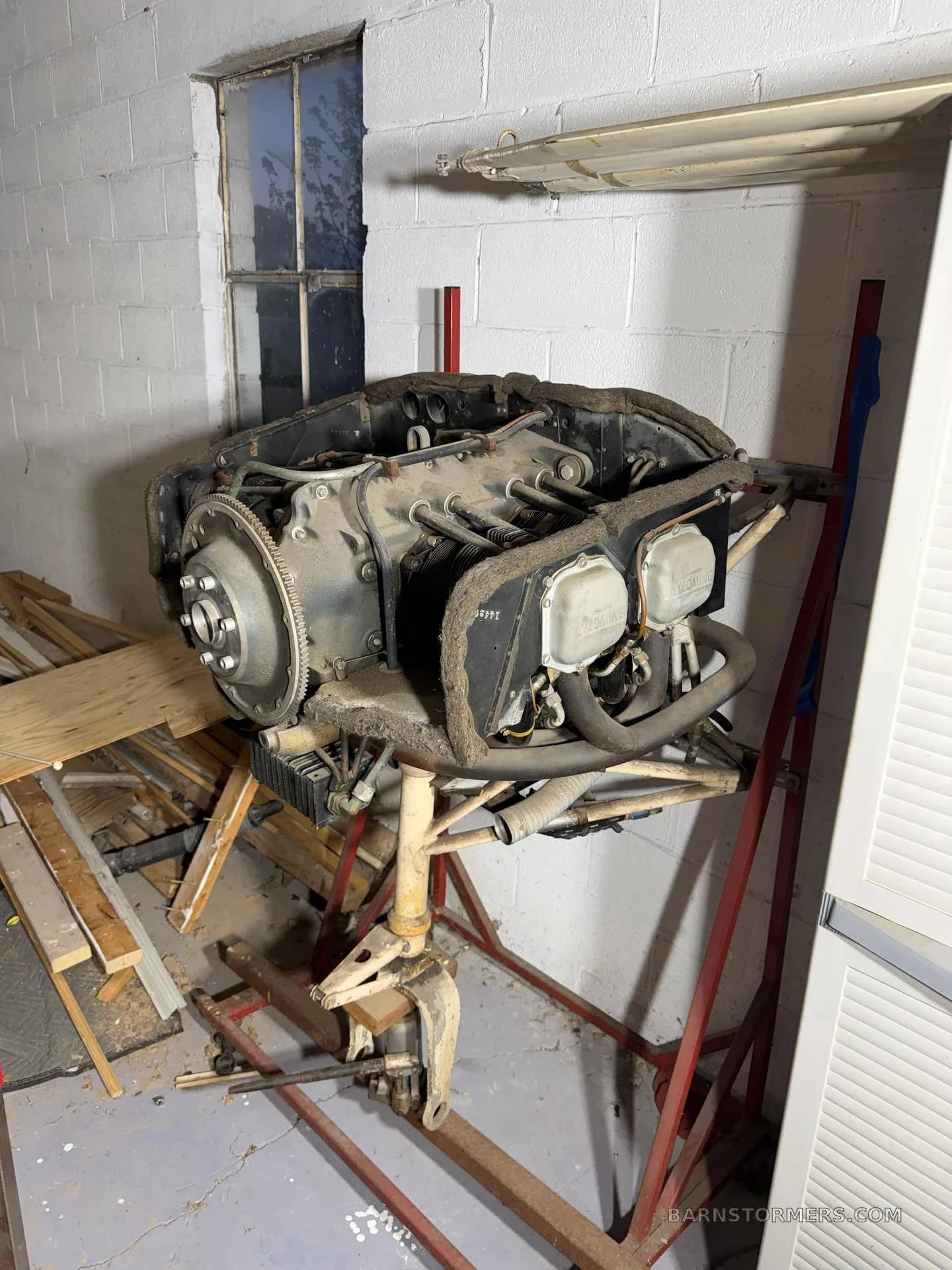 A dusty aircraft engine, likely a Lycoming, mounted on a red stand in a cluttered workshop.