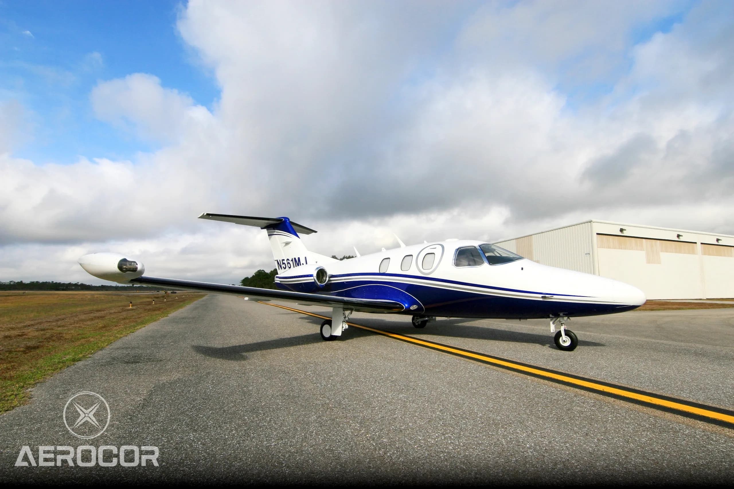 A white and blue Eclipse 500 jet, registration N561MJ, parked on an airfield under a partly cloudy sky.